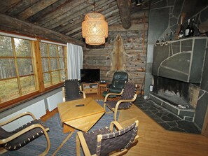 Un interior rústico con chimenea de piedra, muebles de madera y un gran ventanal con vistas a un bosque.
