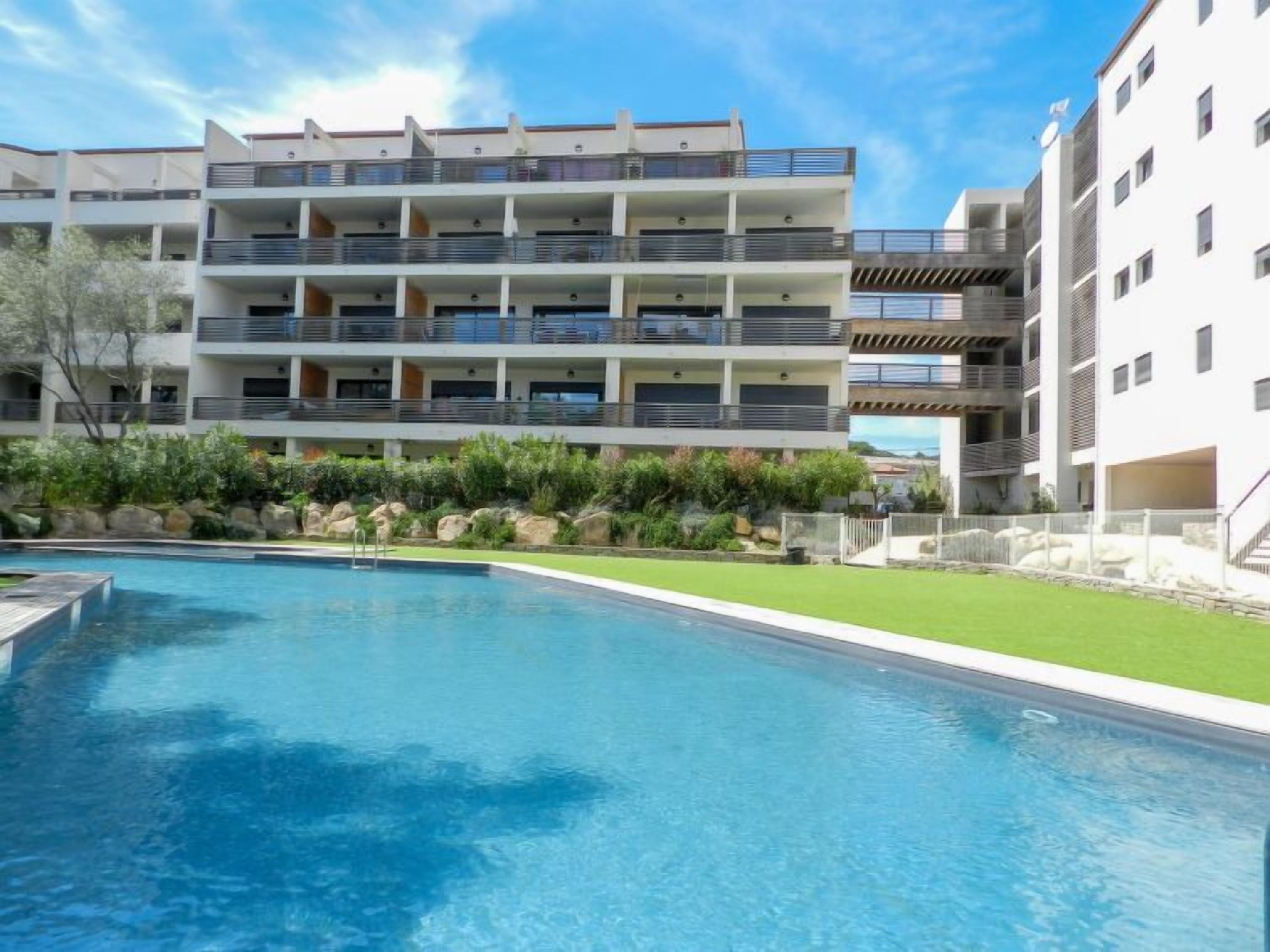 A modern hotel with a pool, multiple balconies, and a well-maintained garden.
