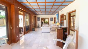 Un interior espacioso con techo alto, una zona de estar central y vistas a través de grandes puertas de cristal.