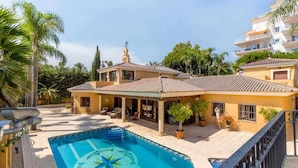 Propiedad residencial con piscina, terraza techada y vista de un edificio vecino.