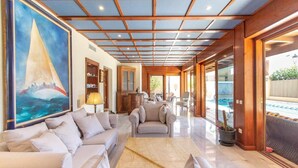 Amplia sala de estar con un cuadro grande de un velero, techo de madera y vista a una piscina.