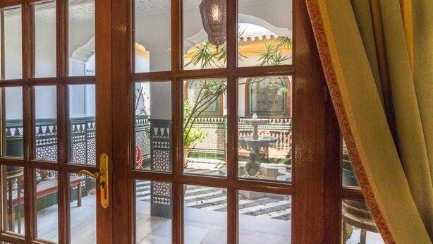 Una puerta de madera con paneles de vidrio, una reja metálica decorada y una estatua de piedra en el patio.