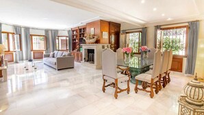 Un amplio salón con una mesa de comedor de cristal, sillas elegantes, un sofá y una chimenea.