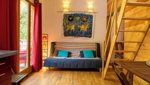 A cozy room with a wooden floor, a bed with patterned bedding, a painting on the wall, and a wooden ladder. - Chalet Jardin Zaza (saint remèze)