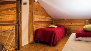 A bedroom with a sloped ceiling, wooden walls, a bed with red bedding, a small stool, and a window. - Chalet Jardin Zaza (saint remèze)