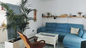 A living room with a blue sofa, a wooden chair, a small white table, and a large potted plant. - ABA DALI GOLDEN (Conil de la Frontera)