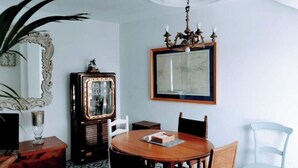 A dining area with a round wooden table, chairs, a chandelier, a large mirror, and a cabinet with glass doors. - ABA DALI GOLDEN (Conil de la Frontera)