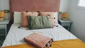 A neatly made bed with multiple pillows and a blanket, two bedside lamps, and a window with daylight. - ABA DALI GOLDEN (Conil de la Frontera)