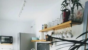 A compact kitchen with a wooden countertop, a built-in sink, a microwave, and a refrigerator. There are shelves above the counter holding various items and a potted plant. - ABA DALI GOLDEN (Conil de la Frontera)