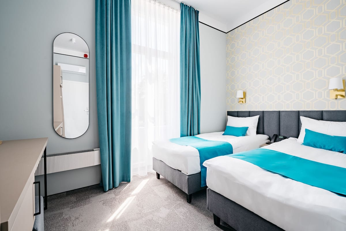 Habitación de hotel con dos camas, un escritorio, un espejo y un radiador.