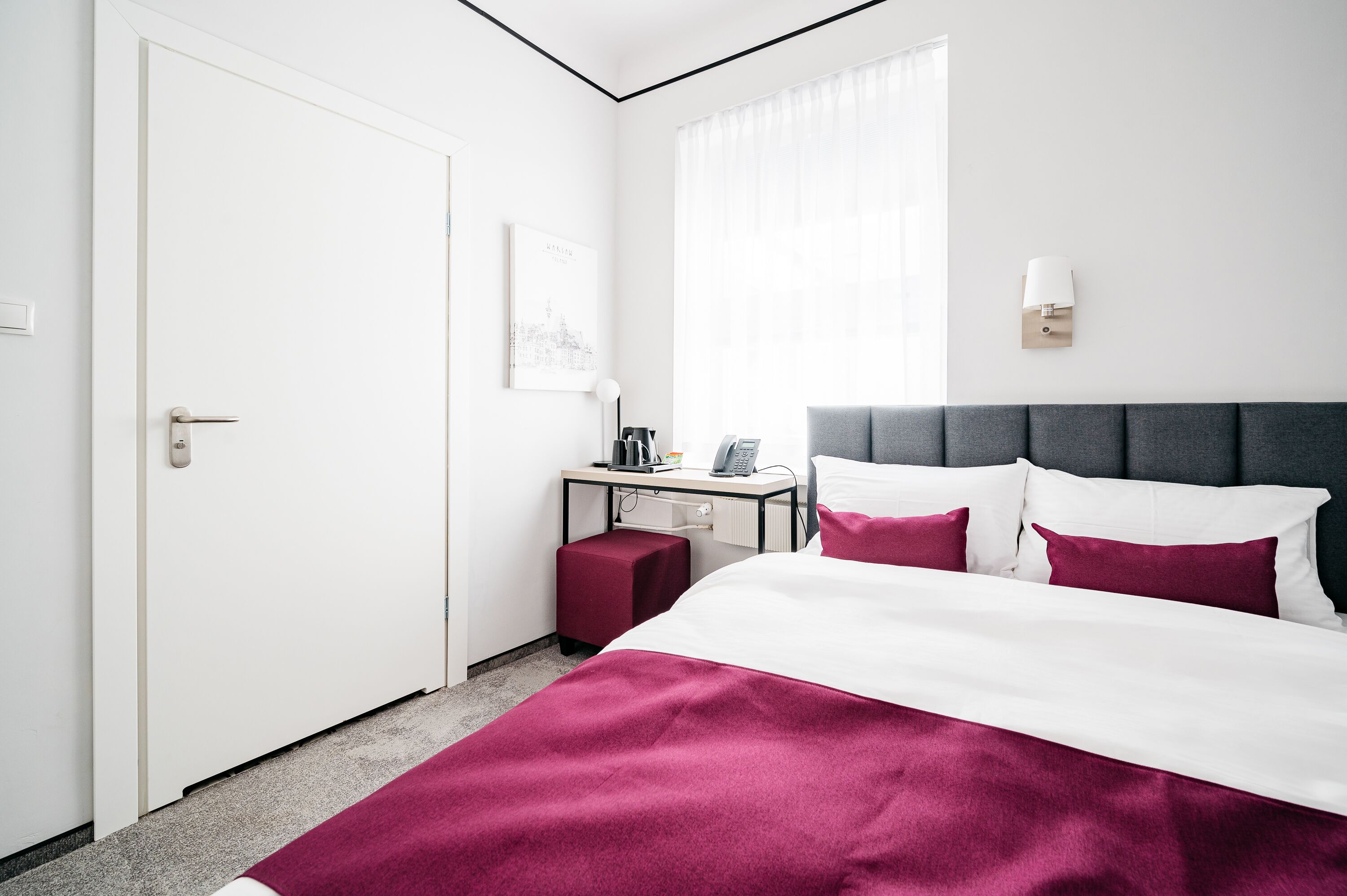 Et hotelværelse med en seng, et skrivebord med lampe, en telefon og et vindue med gardiner.