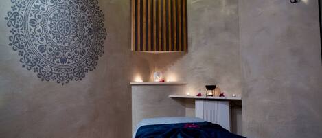 A bedroom with a bed, a wall with a mandala design, a shelf with candles, and a hanging light fixture.