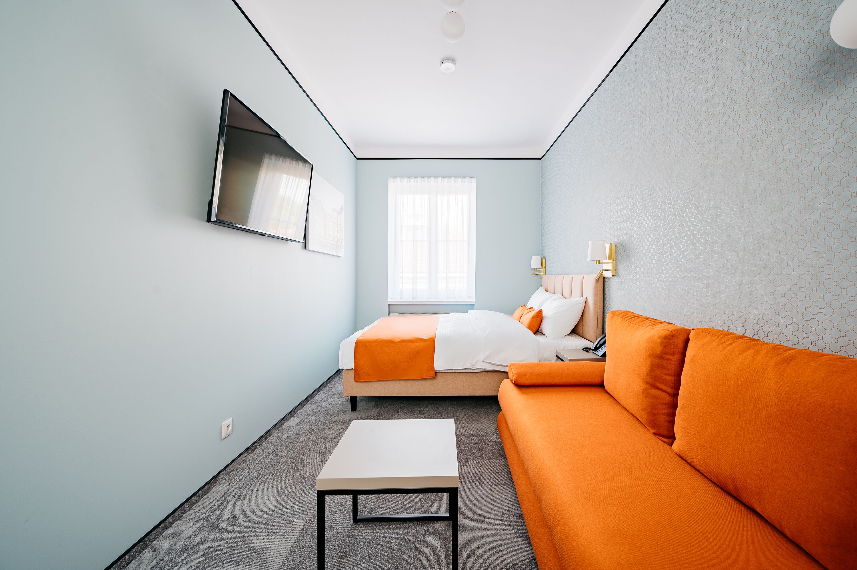 Une chambre d’hôtel moderne avec un lit, un canapé orange et une petite table blanche.