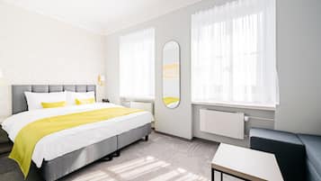 A modern hotel room with a large bed, a bedside table, a chair, and a large window with curtains.