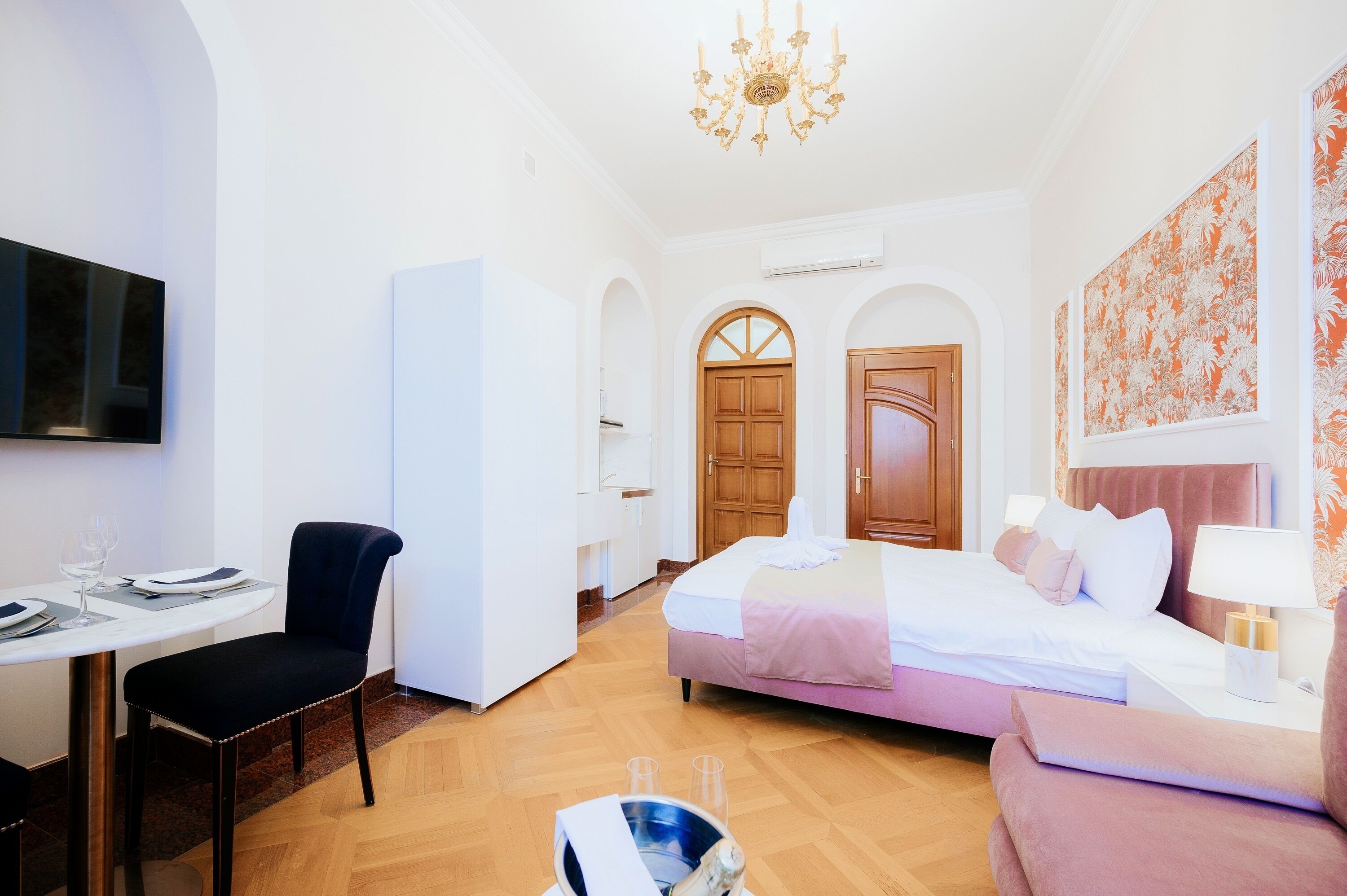 A hotel room with a bed, a desk, a chair, a dining table, and a chandelier.