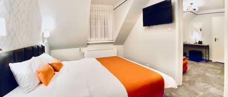 A modern hotel room with a neatly made bed, a flat-screen TV mounted on the wall, and a small desk area with a chair.