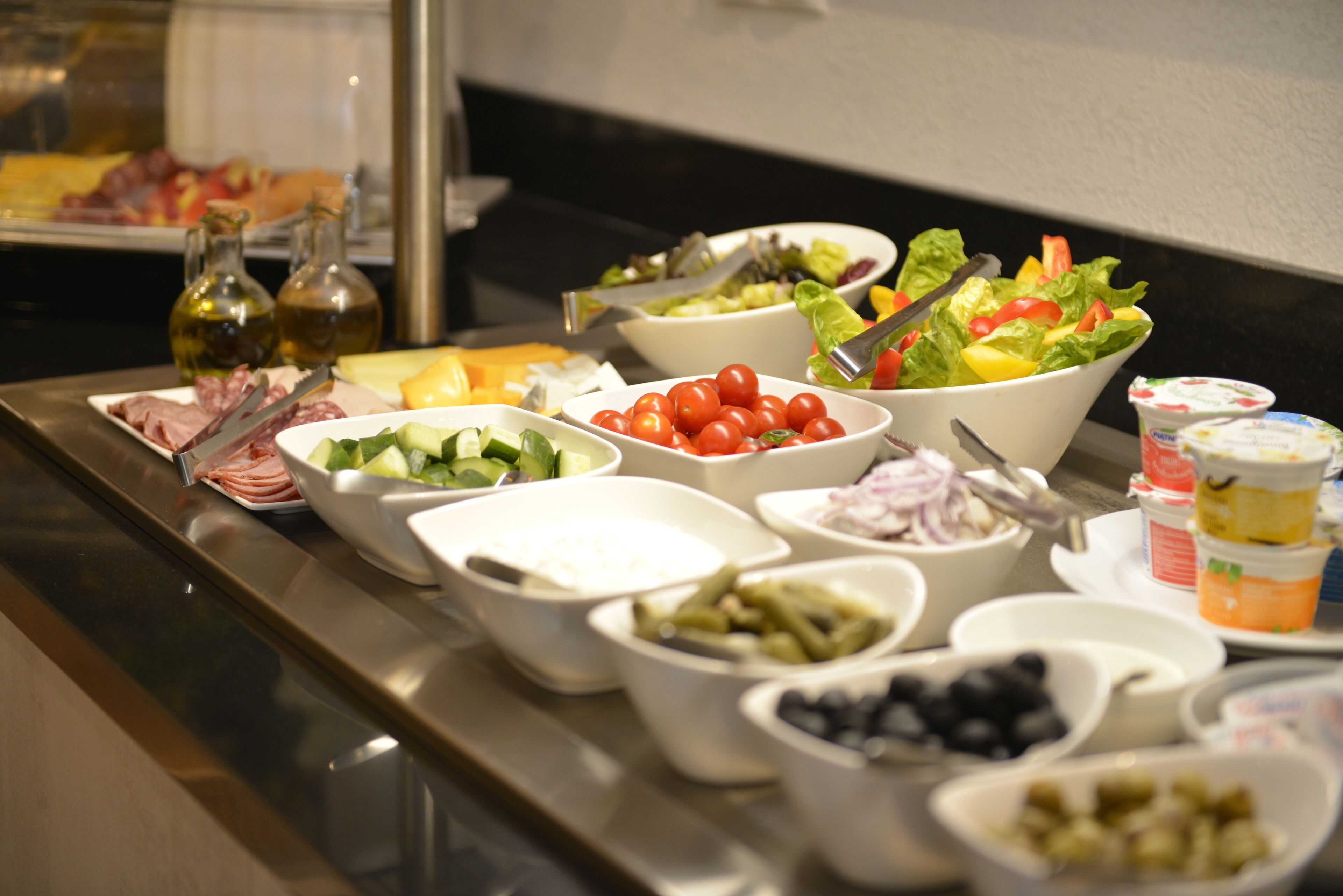 Uma mesa de buffet com diversos alimentos, incluindo saladas, queijos e patês.