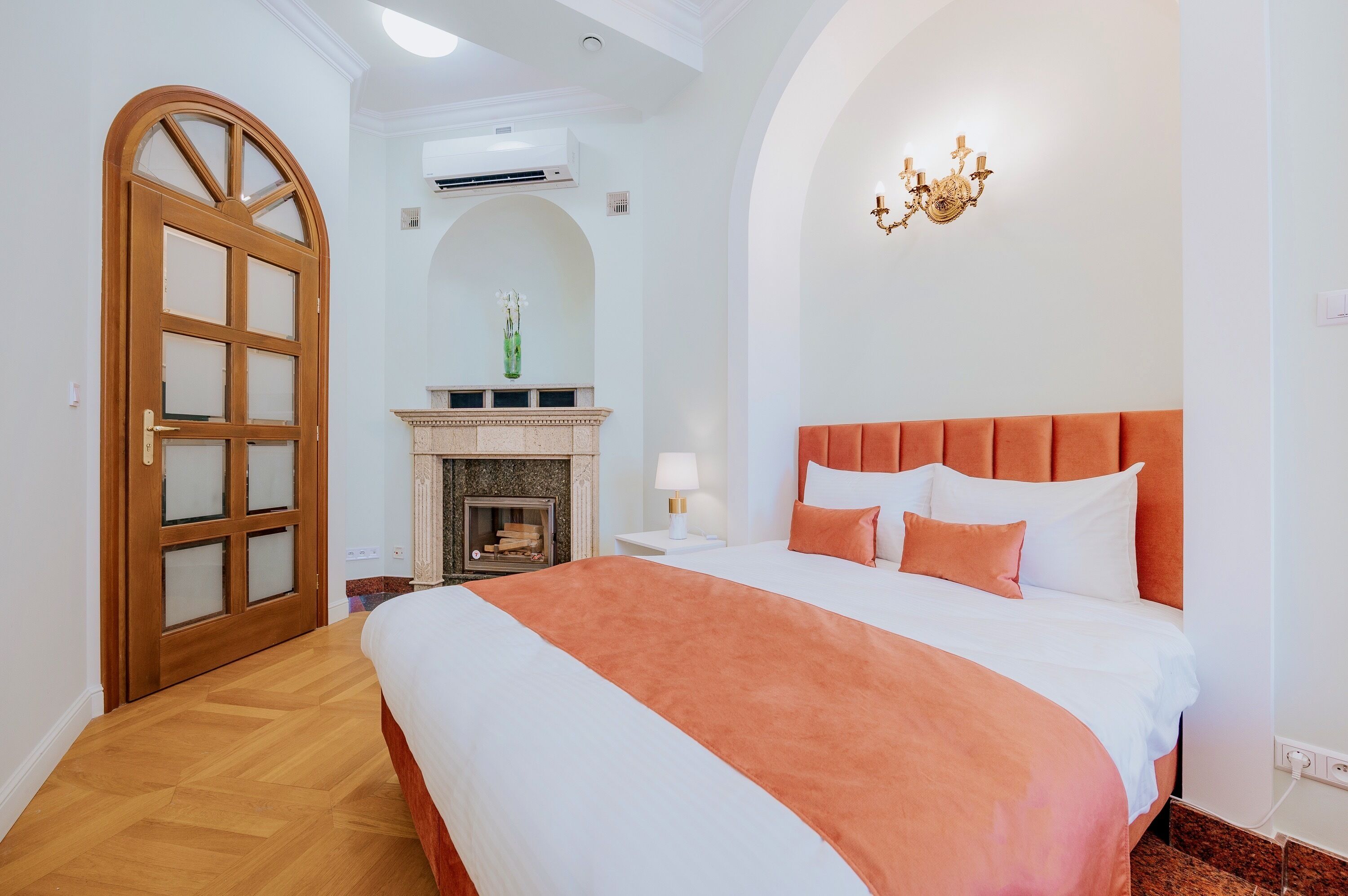 A hotel room with a large bed, a fireplace, a chandelier, and a wooden door.