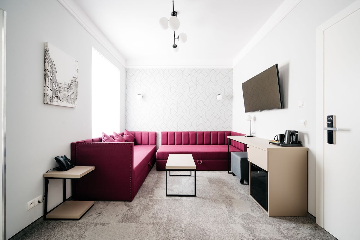 Un espacio habitable moderno y funcional con un sofá rojo, una mesita, un televisor y una cafetera.