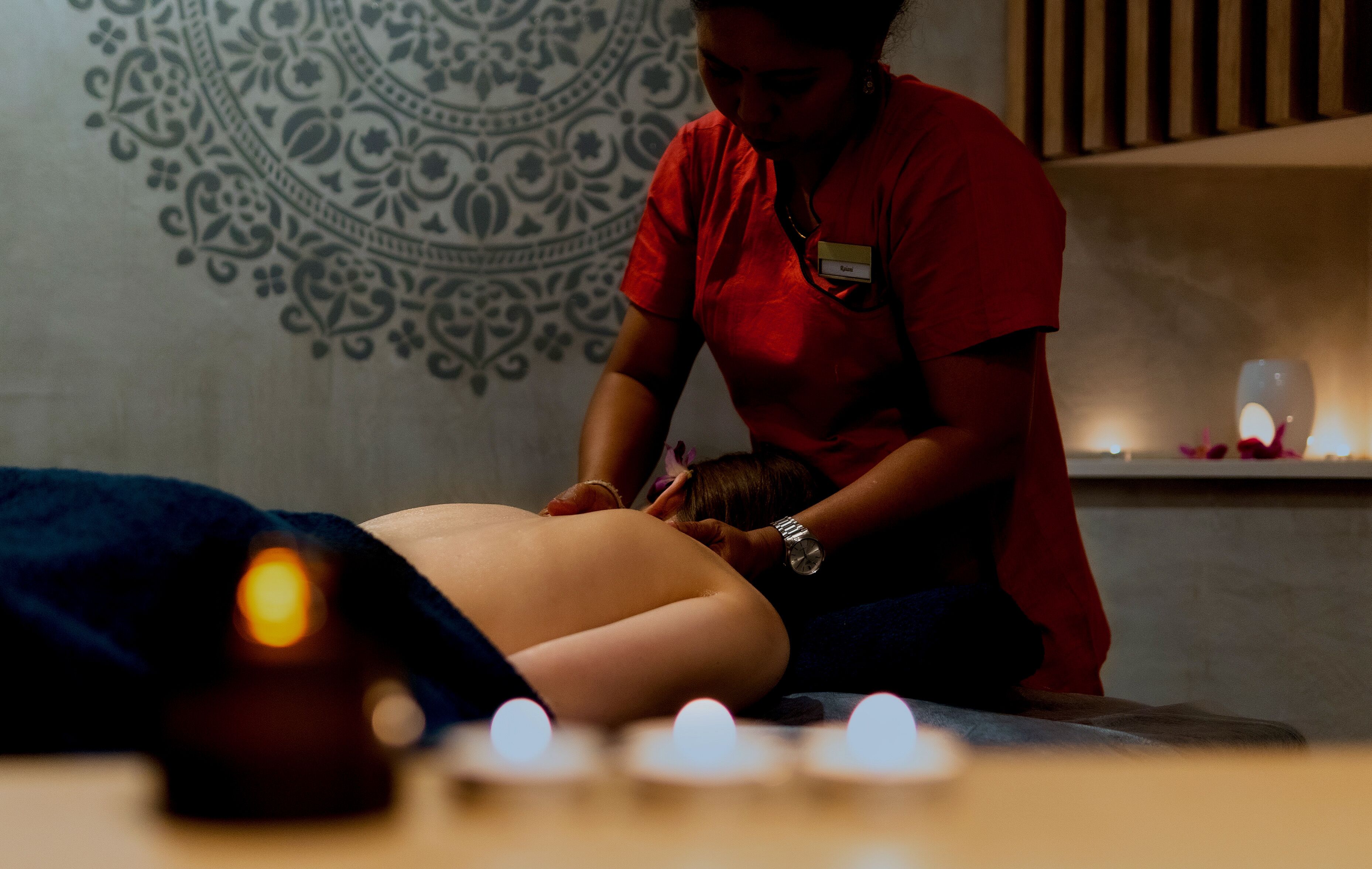 Eine Person erhält eine Massage in einem Raum mit gemusterten Wänden und Kerzen.