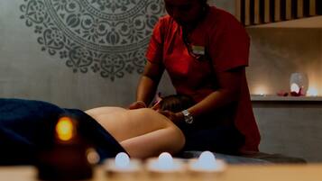 Eine Person erhält eine Massage in einem Raum mit gemusterten Wänden und Kerzen.