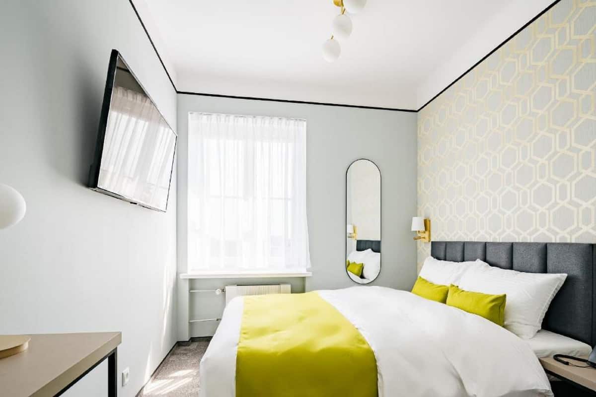 Una habitación de hotel con cama, mesita de noche, espejo y ventana con cortinas.