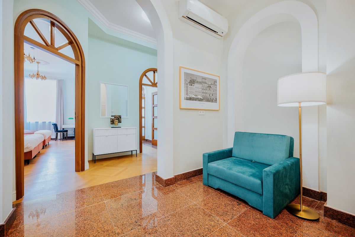 Un hall de hotel con un sofá azul turquesa, una lámpara de pie y un cuadro en la pared.