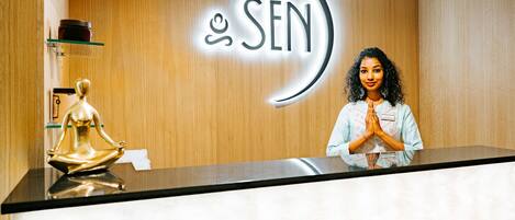 A reception desk with a wooden backdrop, a logo with the text "SEN", and a golden statue of a seated figure.