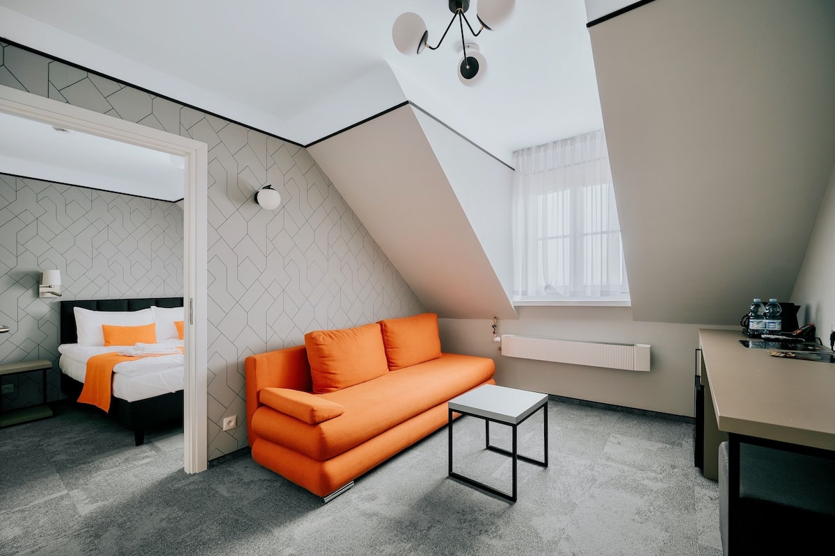 Una habitación moderna con una cama, sofá naranja y una pequeña mesa.