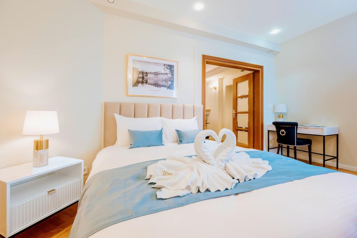 Habitación de hotel con cama, escritorio, silla, lámpara y un cuadro en la pared.