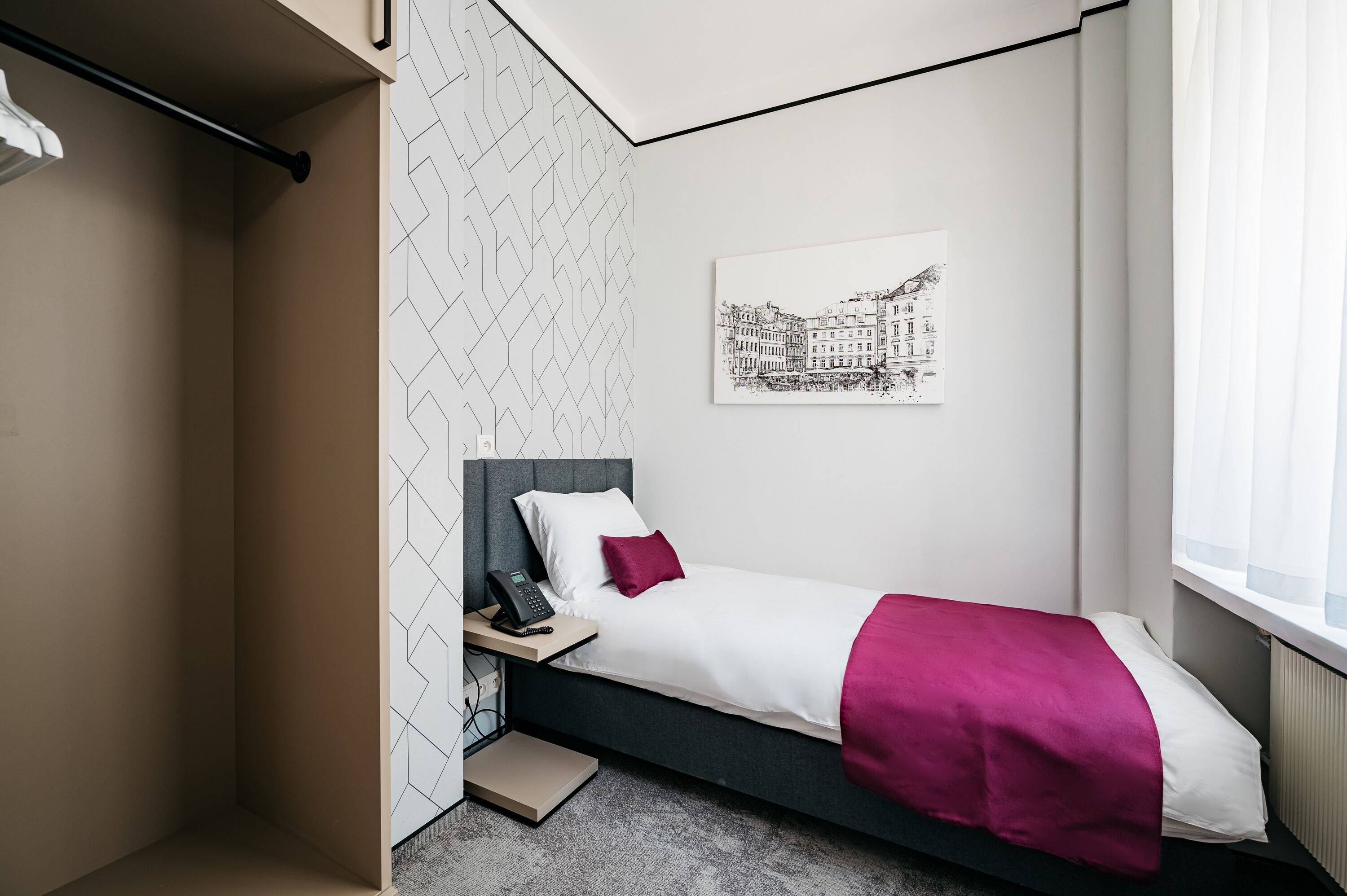 Une chambre à coucher comprenant un lit, une table de chevet, un téléphone, une fenêtre et une œuvre d’art accrochée au mur.