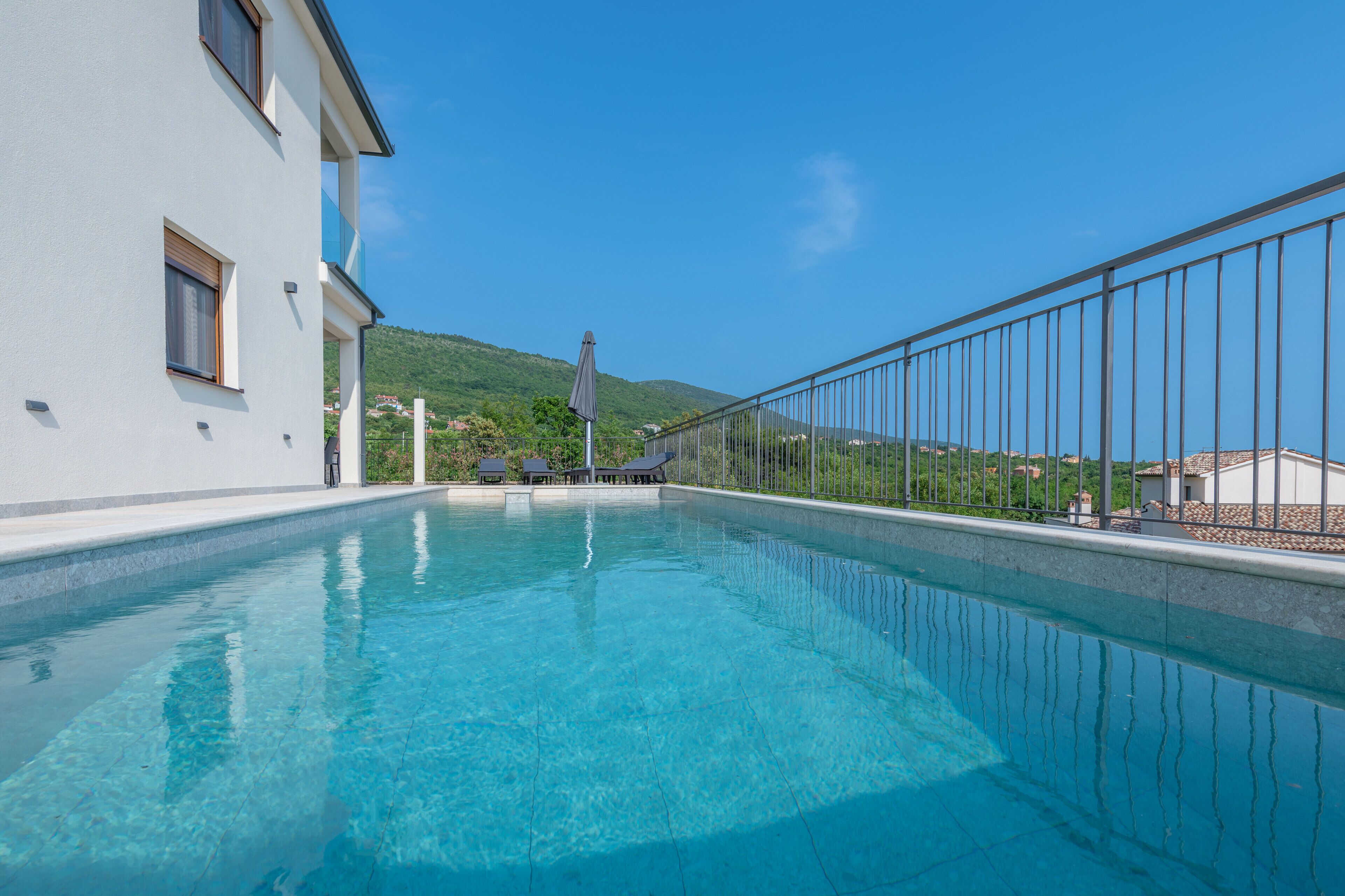 Une piscine à l’eau d’un bleu limpide, avec une rambarde métallique d’un côté, et une vue sur une montagne en arrière-plan.