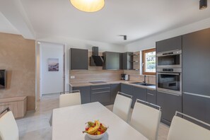 Een moderne keuken met grijze kastjes, een ingebouwde oven en een eethoek met een tafel en stoelen.
