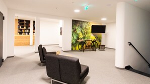 A modern interior with a sofa, a bookshelf, a bicycle, and a wall-mounted TV. - Self-Check-in Hotel VinoQ Zistersdorf (Zistersdorf)