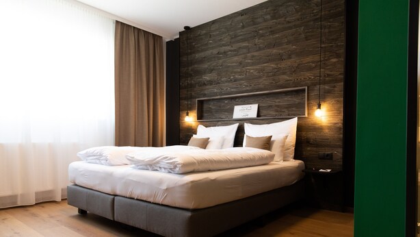 A modern hotel room with a large bed, wooden headboard, and a green accent wall. - Self-Check-in Hotel VinoQ Zistersdorf (Zistersdorf)
