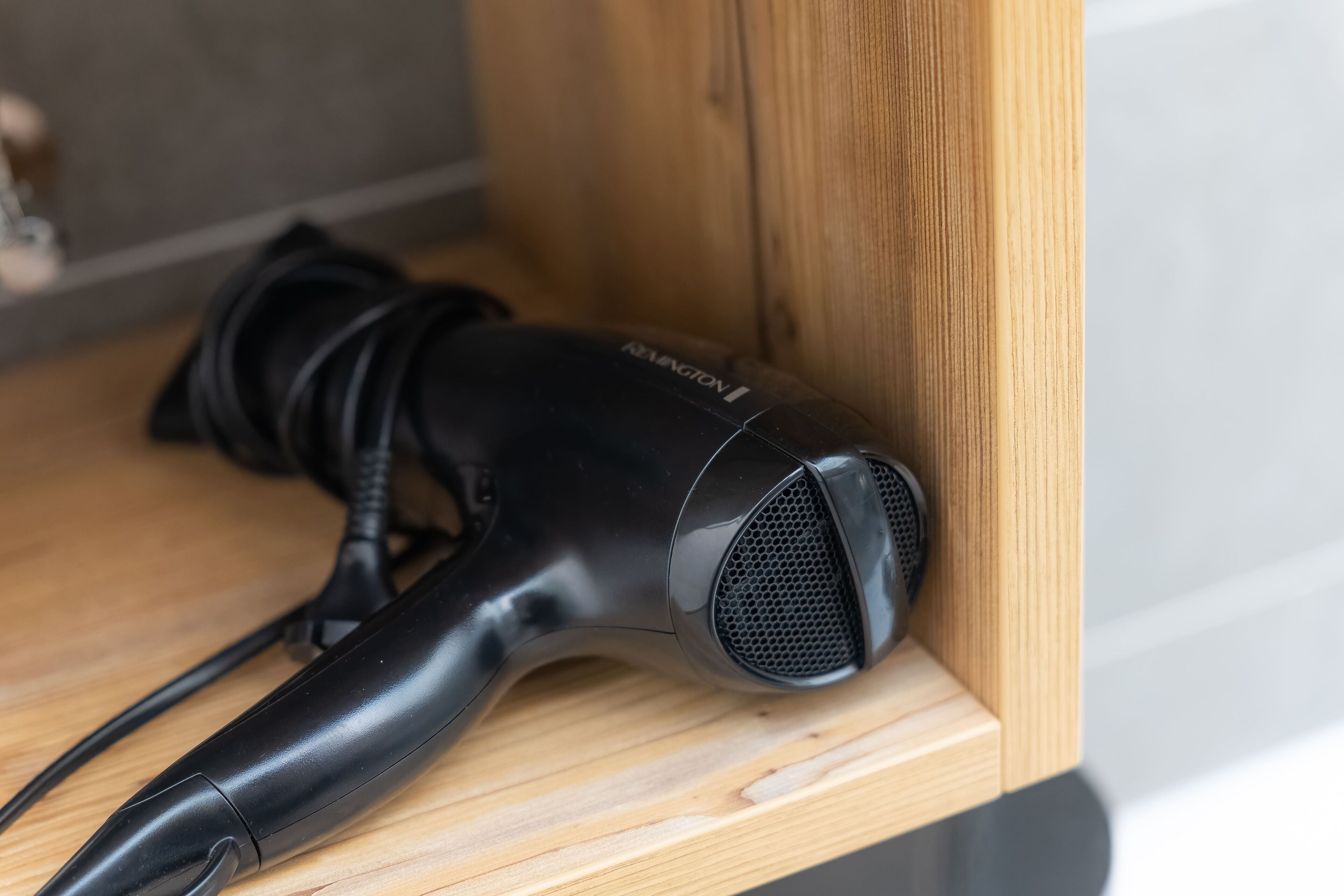 A black hairdryer on a wooden shelf.
