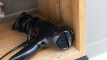 A black hairdryer on a wooden shelf.