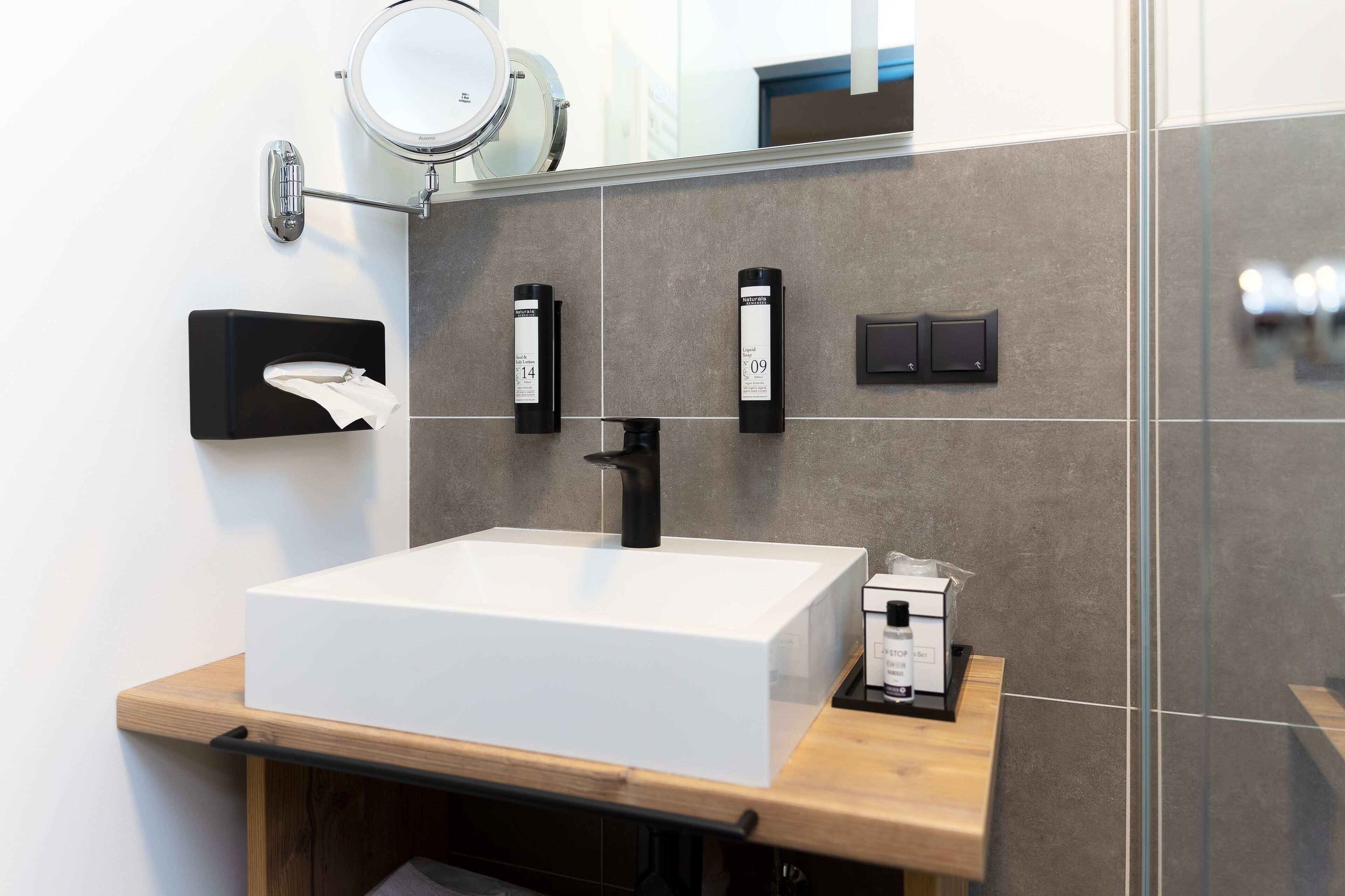Un baño moderno con un lavabo blanco, un espejo y dos dispensadores negros en la pared.