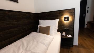 Un lit bien fait, avec une tête de lit en bois, une table de chevet sur laquelle se trouvent un téléphone et un livre, et une lampe fixée au mur.