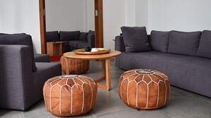 Un salón moderno con un sofá gris, dos otomanas, una mesa redonda de madera y un espejo que refleja la estancia.