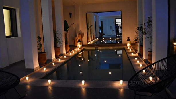 Un área de piscina interior moderna con un banco largo, velas y plantas en macetas.