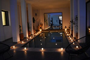 Un área de piscina interior moderna con un banco largo, velas y plantas en macetas.