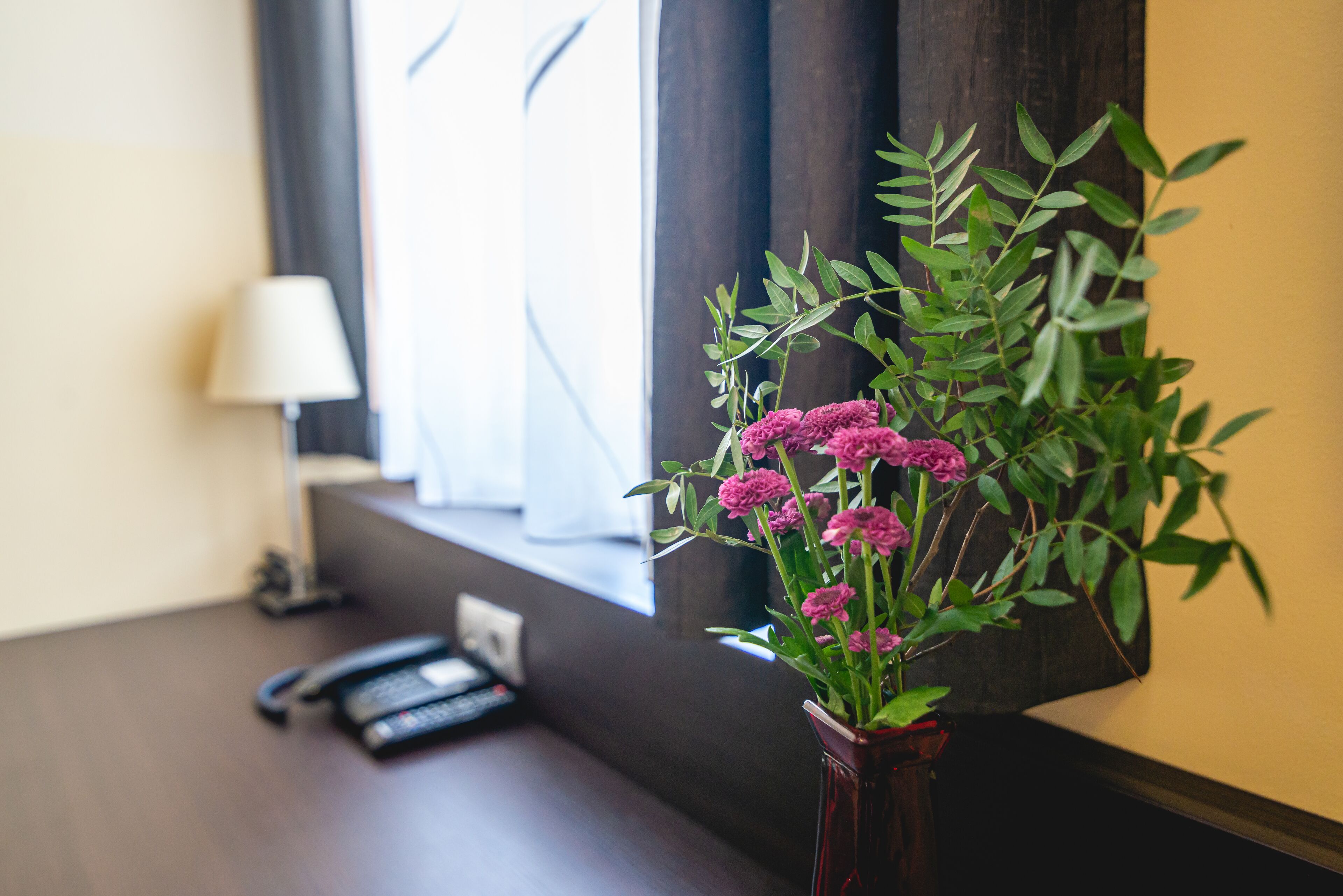 Un escritorio con un jarrón de flores, una lámpara y un teléfono.