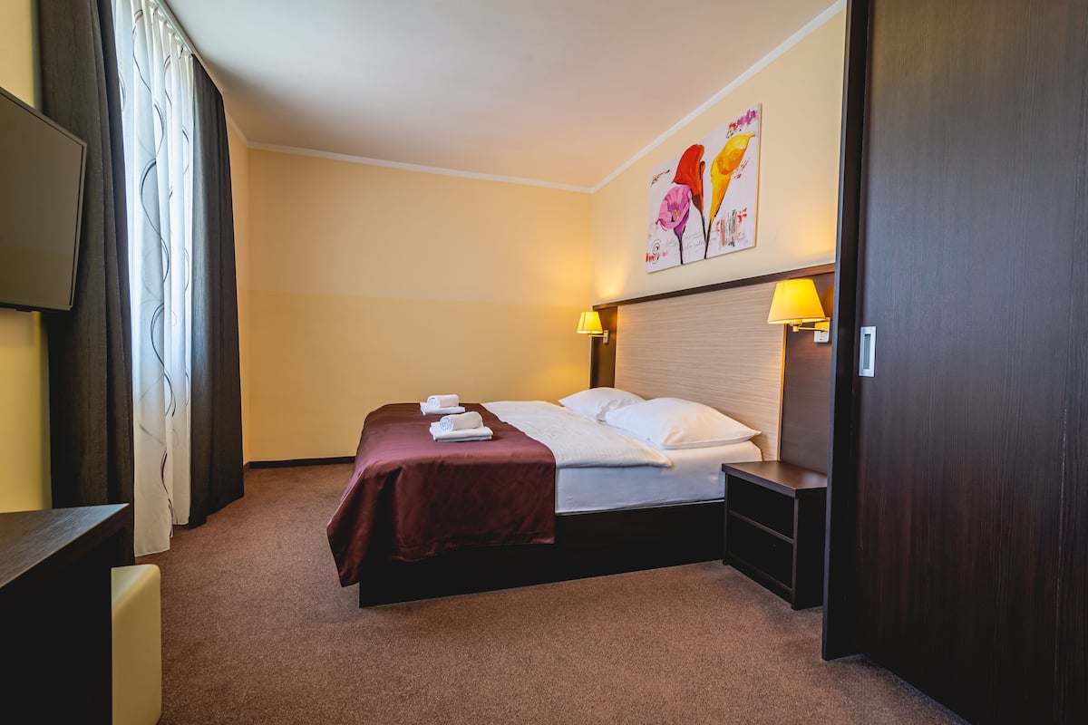 Een hotelkamer met een bed, bedlampen, een flatscreen televisie en een schilderij aan de muur.