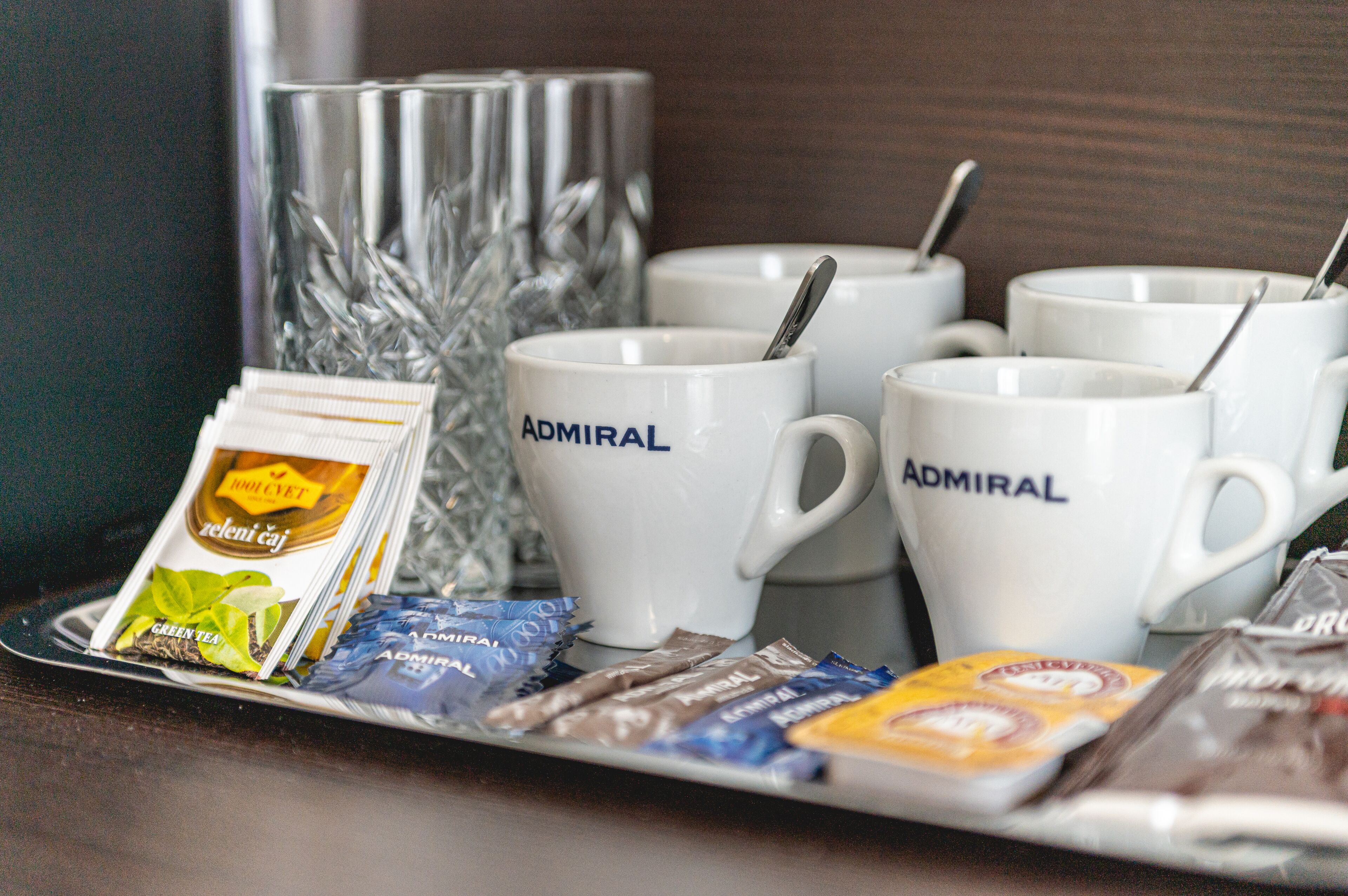 A tray with multiple white mugs labeled "Admiral," a glass container, and various packaged snacks.
