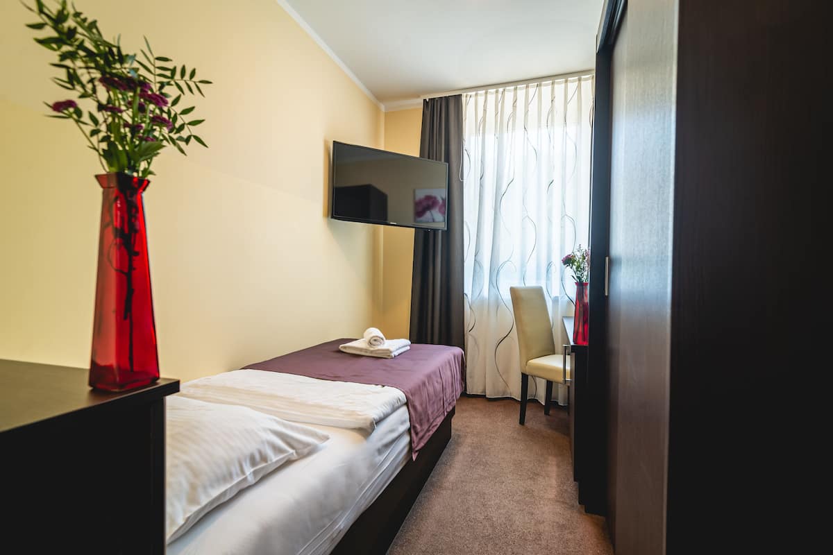 Een hotelkamer met een bed, een aan de muur bevestigde televisie, een rode vaas met bloemen en een stoel.