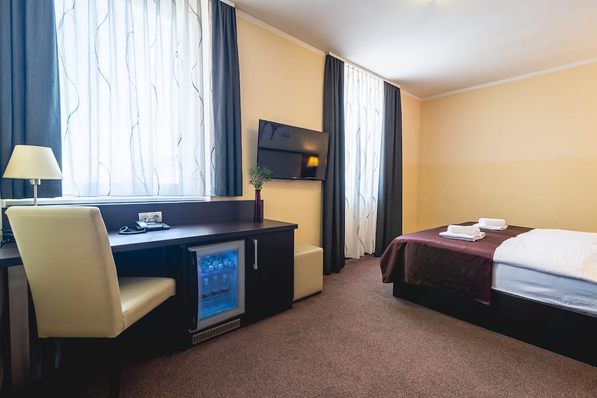 Een hotelkamer met een bureau, stoel, bed, televisie en een kleine koelkast.