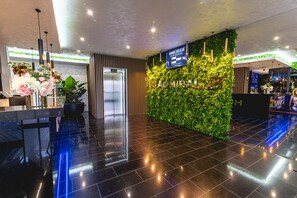 A modern hotel lobby with a reception desk, a digital sign, a green wall with plants, and a polished black floor. - Casino & Hotel ADMIRAL Ptuj (Ptuj)