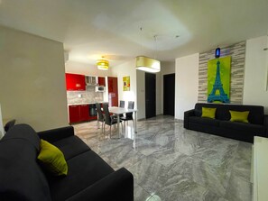 A modern living room with a black sofa and a dining area with a white table and chairs. - Red 1: One-Bedroom Apartment in St. Julian's (Swieqi)