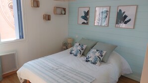 Une chambre à coucher avec un lit, une fenêtre, une horloge murale et des reproductions botaniques encadrées.